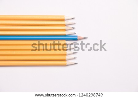 One blue pencil among several orange pencils on white background demonstrating leadership, difference, uniqueness and ambitions
