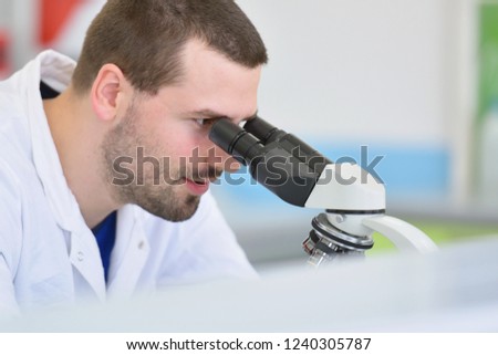 Young male scientist looking through a microscope in a laboratory doing research, microbiological analysis, medicine.