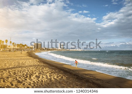 Girl with a bag walking on the beach on sunny day. Stylish hipster near the waves on the sea. Ocean coast. Holiday travel concept. Barcelona Spain.