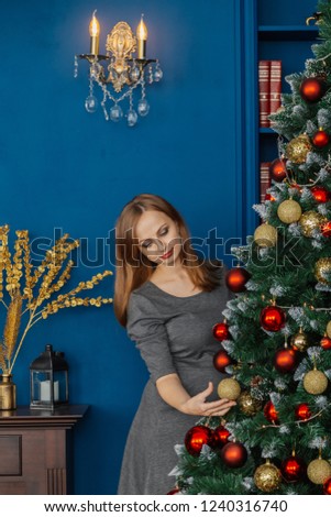 Very beautiful girl stands near the Christmas tree and touches toys.
