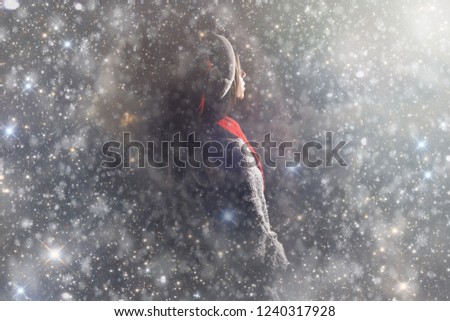 Merry Christmas and happy new year! Adorable female hold present in hands. Close portrait on gray background. Girl in santa hat and sweater look on light under snow falling in night