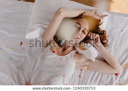 Wonderful caucasian girl lying in bed with gently smile. Indoor overhead shot of adorable white woman posing with eyes closed.