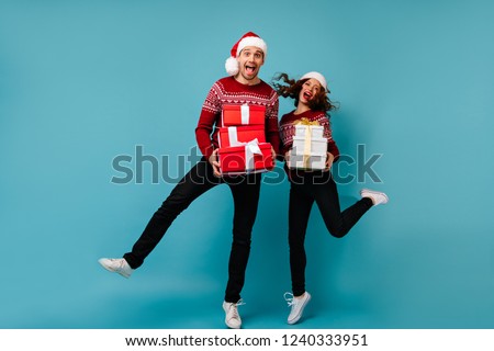 Carefree young people jumping with new year presents. Refined slim girl in santa claus hat having fun with boyfriend in christmas.
