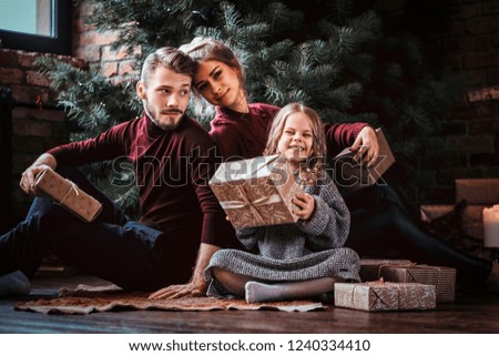 Attractive family opens presents while sitting on a floor next to the Christmas tree. 