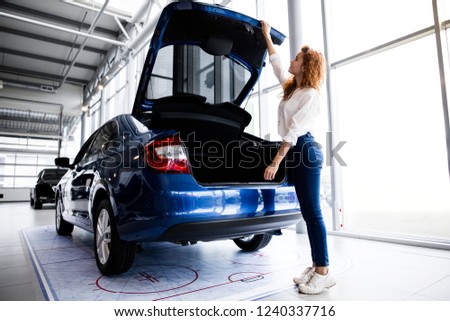 Redhead girl inspects the trunk of a new car in the showroom