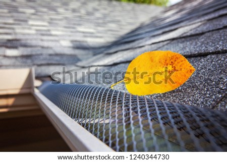 Plastic guard over gutter on a roof with a leaf stuck on the outside Royalty-Free Stock Photo #1240344730