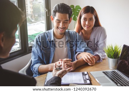 new house / home moving and relocation concept. Happy asian couple receiving apartment key from real estate agent / realtor.