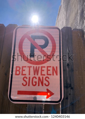 No Parking Between Signs with arrow and sunlight in the blue sky