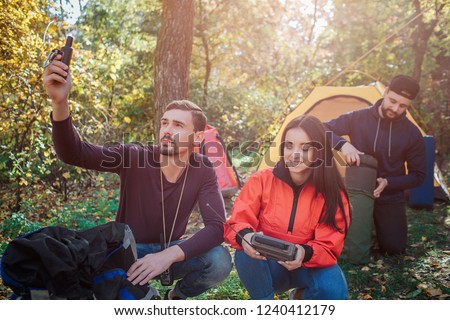 Picture of young beautiful woman holds radio in hands. First guy has satellite phone. Another gets sleeping bag from cover.