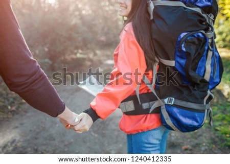 Lovely picture of young man and woman holding hands together. She has backpack on back and map on hands. They walk together.