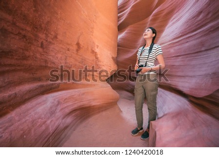 full length of young lady traveler holding camera cheerfully looking up to the sunny sky. asian girl standing in lower antelope canyon. female lens man with slr camera joyfully enjoying the view.
