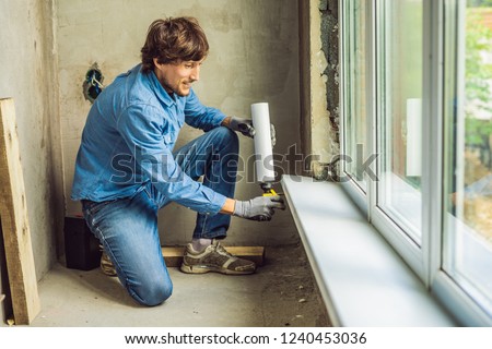 Man in a blue shirt does window installation. Using a mounting foam