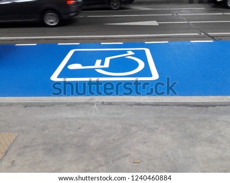 Bright blue disabled parking sign on the road with blurred car.