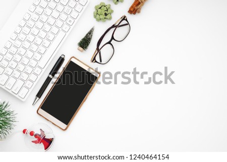 Merry Christmas and Happy new year office desk table, workspace office with wireless keyboard, black screen smartphone, pen, glasses and Christmas ornaments decoration. Top view with copy space.