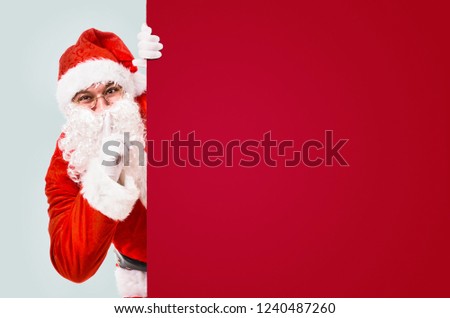 Santa Claus with finger on lips asking for silence with colorful advertisement board and copy space