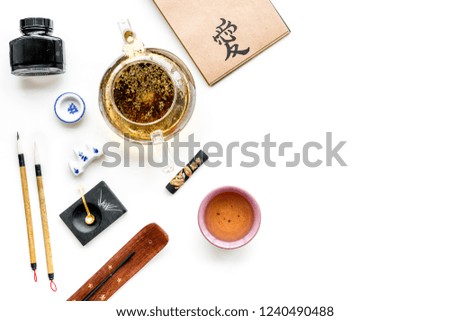 Chinese or japanese calligraphy pattern. Hieroglyph love in craft paper notebook, writing accessories, teapot and cup of tea on white background top view copy space