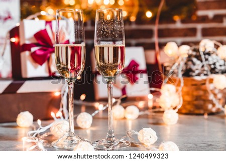 Two champagne glasses in front of christmas presents and sparkling background