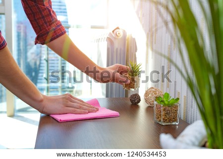 A housewife in a shirt is cleaning the house, wipes dust from the table with a cleaning rag. Household chores Royalty-Free Stock Photo #1240534453