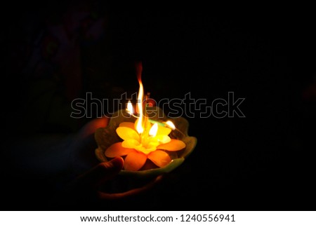 Loy Krathong festival, Blurred hand and candle krathong with fire. dark low light with noise. Spa candle flower shape. Fire spiritual ceremony witch concept. copy space.
