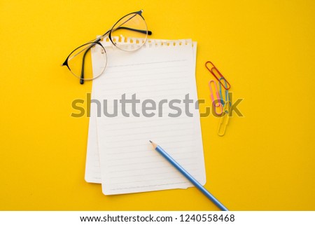 empty paper of notebook eyeglasses and pencil on color background.