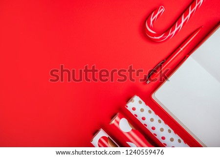Christmas flatlay with clean note pad, red pen, wrapping paper and candy canes on the bright red background.
