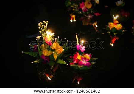 Loy krathong, blurred Flowers krathong with candle light floating in River, dark low light with noise, Thai culture traditional.