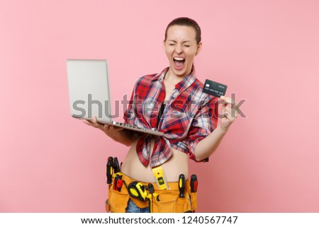 Handyman woman user with kit tools belt full of instruments working on laptop pc computer, holding credit card isolated on pink background. Female in male work. Renovation online shopping concept