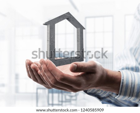 Cropped image of businessman in suit keeping stone house symbol in hands. Mixed media