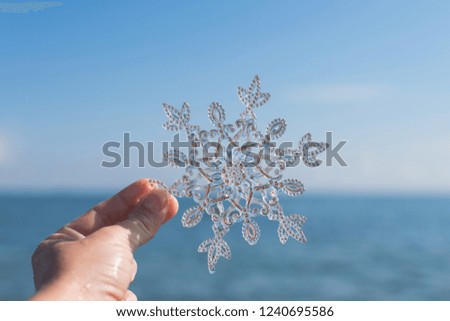 Female hand with sparkling huge snowflake on the sea background. Concept of Winter and Christmas vacation on the beach and resort.