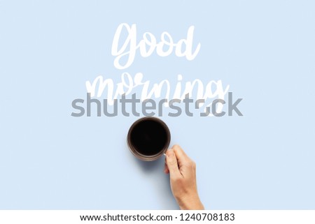 Hand holding a cup with hot coffee on a blue background. Breakfast concept with coffee or tea. Good morning, night, insomnia. Flat lay, top view