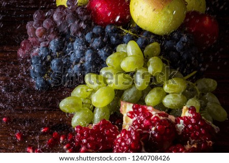 Grapes of several varieties, pomegranates, pomegranate seeds, apples on a wooden background with water splashes. Fresh fruit concept, new crop