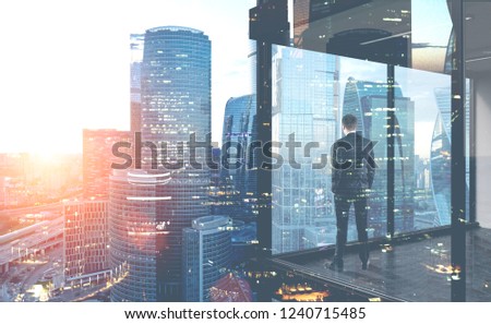 Rear view of young businessman looking at cityscape from his office window. Concept of business planning. Toned image double exposure of city