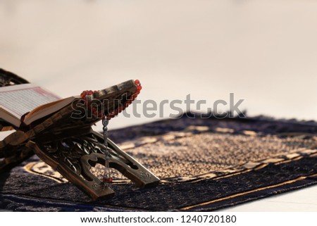 Rehal with open Quran and Muslim prayer beads on rug indoors. Space for text Royalty-Free Stock Photo #1240720180