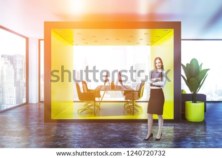 Businesswoman in yellow and wooden open space office with long wooden computer table with black and wooden chairs and gray sofa standing in the lobby. Toned image