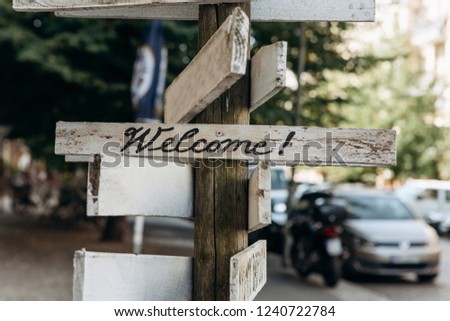 Wooden sign on the street - Welcome. Blurred street in the background.