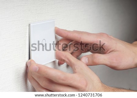 the guy sets the glass cover on the touch switch on the white wall, hands close up