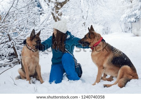 Young woman wearing blue ski suit is sitting on the ground in the snow with two brown dogs in winter 