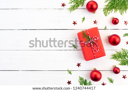 Christmas background concept. Top view of Christmas green and red gift box with spruce branches, pine cones, red berries and bell on white wooden background.