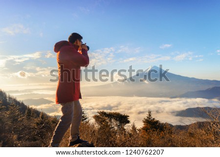 Asian photographer taking landscape photos of Mountain Fuji with morning mist or fog at sunrise in Fujikawaguchiko, Yamanashi, Japan. Landscape with hills.