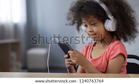 Adorable African girl child wearing earphones, listening to music on cellphone