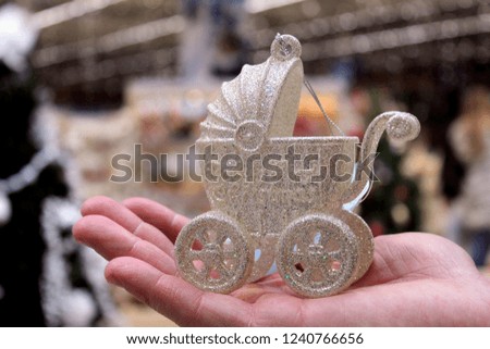 Christmas toy in the form of a baby carriage white closeup in the hands of a man, selective focus.