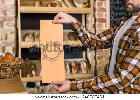 male seller holding paper menu in hands at bakery