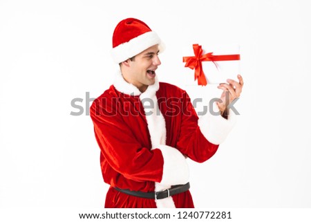 Portrait of joyous man 30s in santa claus costume and red hat holding present box isolated on white background in studio