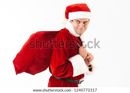 Portrait of tricky man 30s in santa claus costume and red hat walking with gift bag over shoulder isolated on white background in studio
