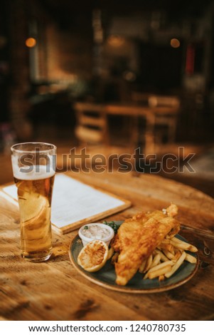 Fish and chips plate and pint of beer on a wooden table at the pub. Royalty-Free Stock Photo #1240780735