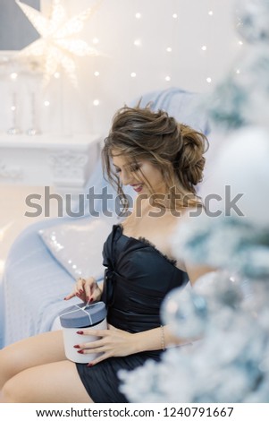 Very beautiful and happy girl sitting on the sofa in the New Year's room and opens a gift.