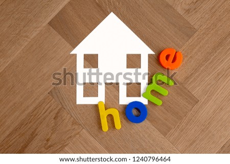 House paper cut out symbol white on wooden floor background with colourful plastic lettering spelling word home