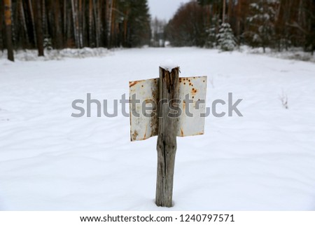 Old tin plate on a wooden pole in the winter forest
