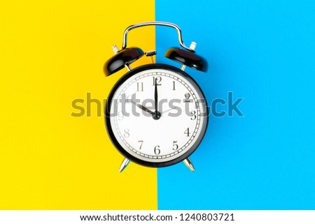 Black alarm clock on color block yellow and blue background