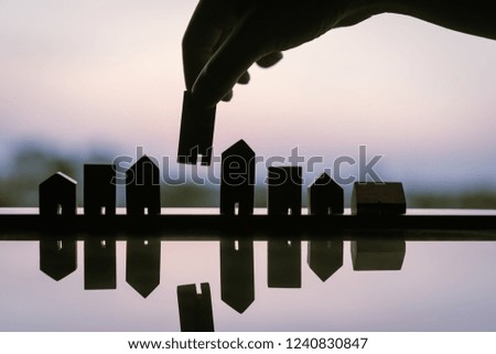 Silhouette of hand choosing mini wood house model from model and row of coin money on wood table, selective focus, Planning to buy property. Choose what's the best. A symbol for construction ,ecology.